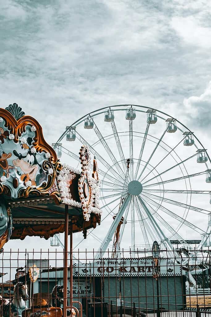 Captivating view of a Ferris wheel and ornate carousel against a cloudy sky in Rhyl, Wales.